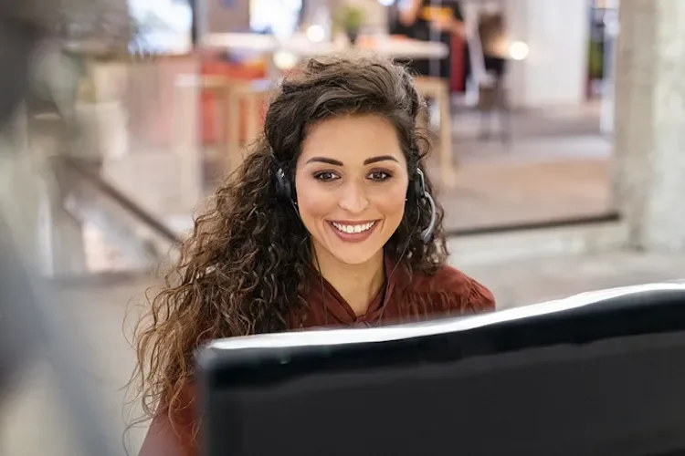 person smiling at a computer screen, wearing a headset