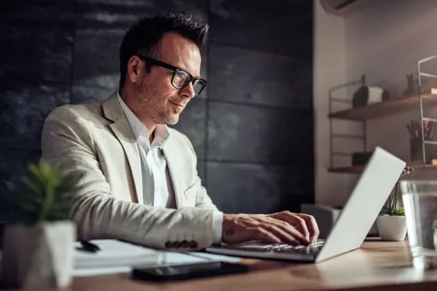 Man with glasses wearing a tan suit accessing a laptop