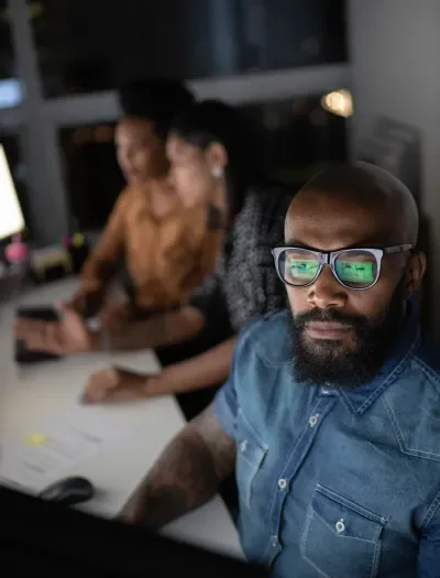 A man with glasses working hard at a computer
