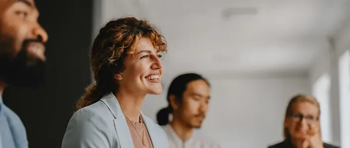People in a meeting, smiling, engaged in conversation, with a bright, modern setting.